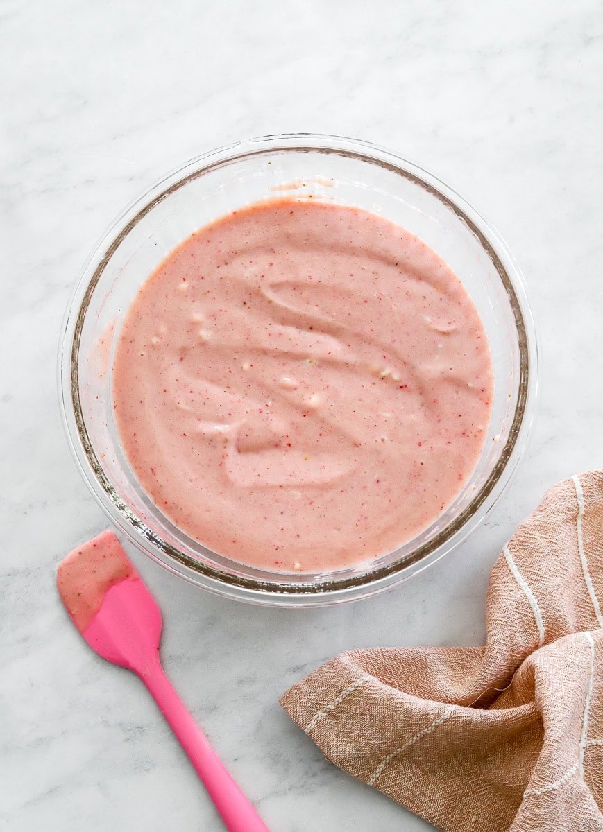 Yogurt mixed with strawberry puree in a glass bowl.