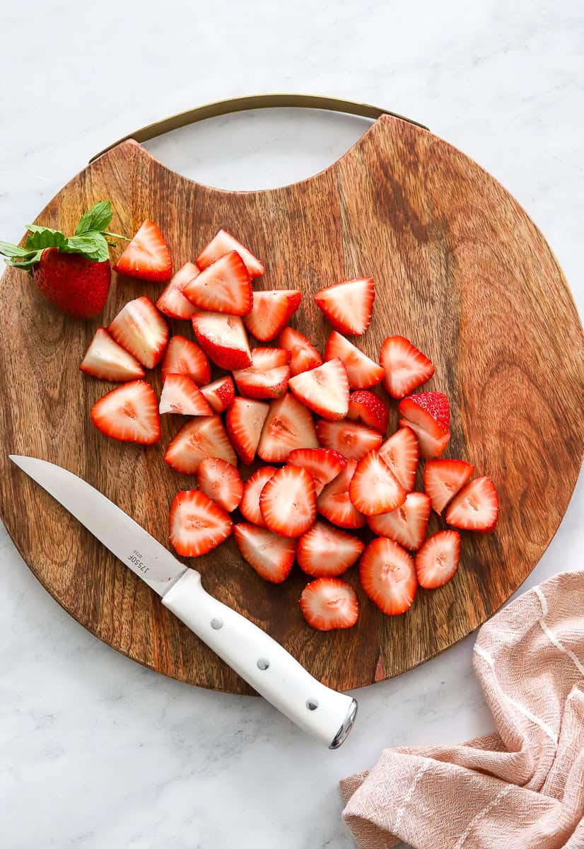 Chopped strawberries on a wood cutting board with a white handled knife on the board.