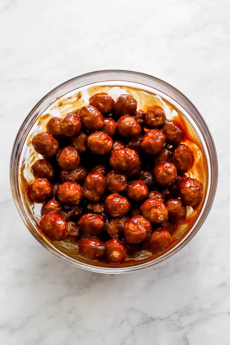 Meatballs tossed in BBQ sauce in a round glass bowl. 