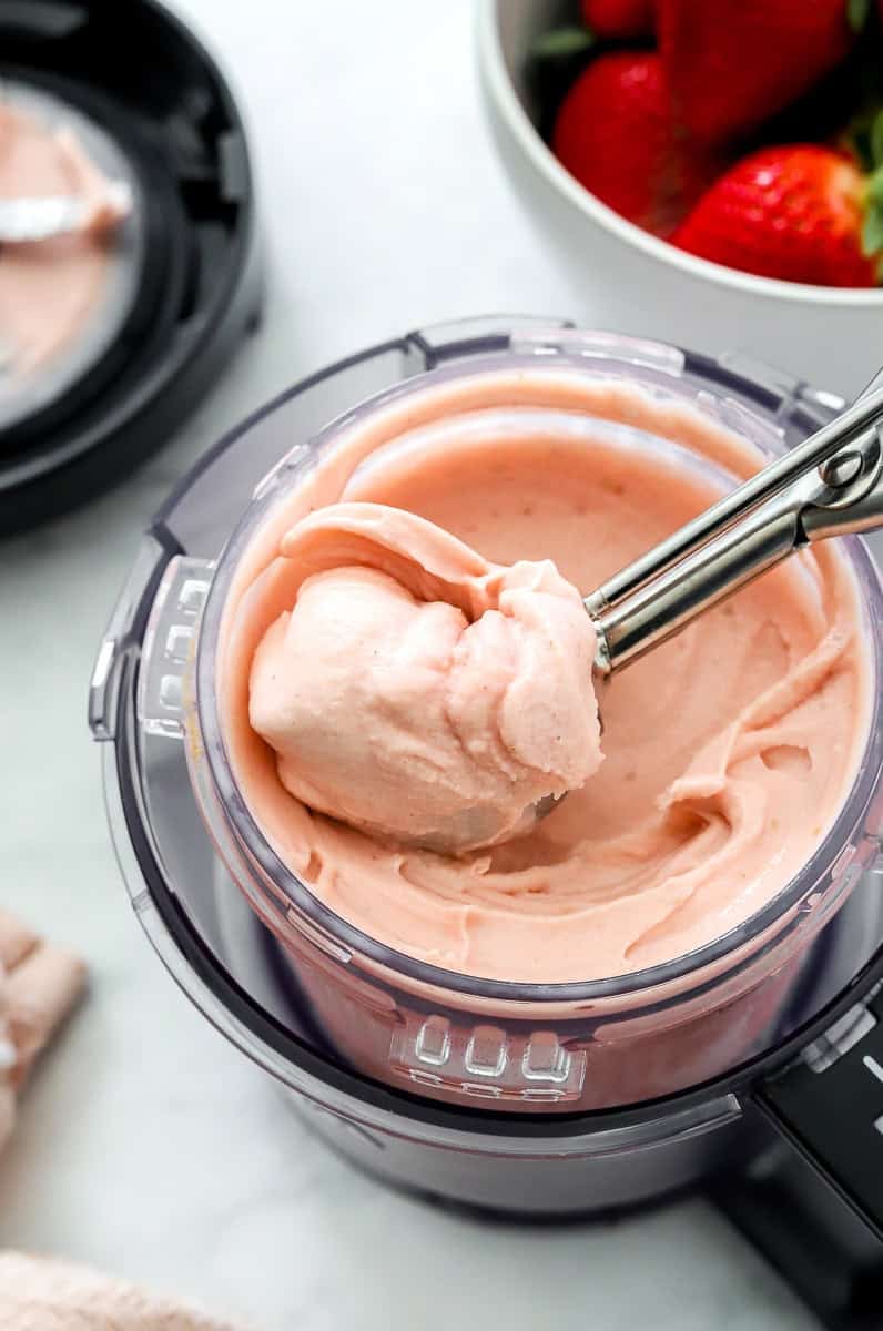 Ninja creami strawberry ice cream in pint container with ice cream scoop in it. 