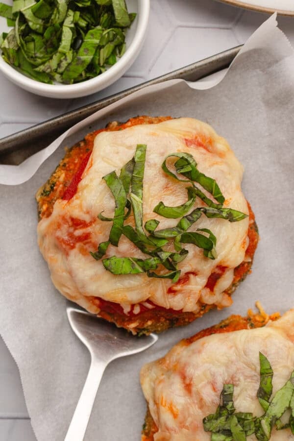 Cooked portobello mushroom parmesan topped with chopped herbs with another one in front of it.