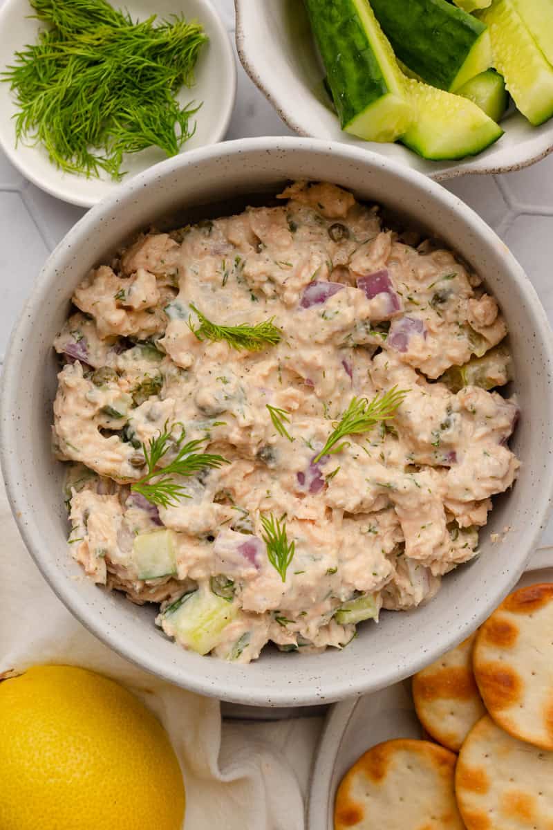 Round bowl filled with creamy salmon salad with veggies and crackers around it. 