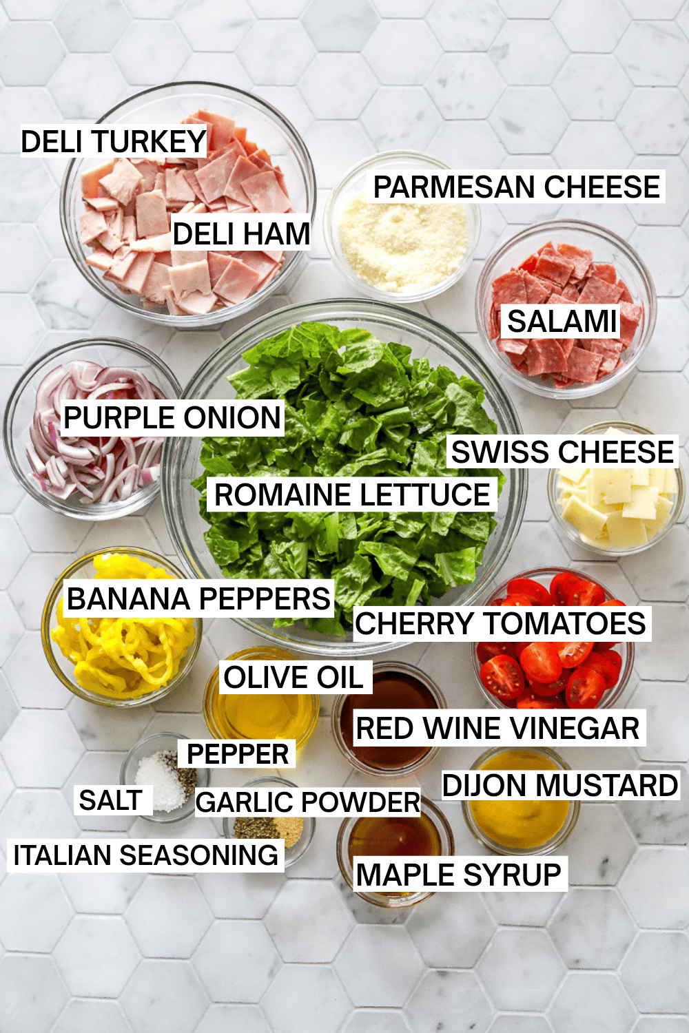Ingredients for a grinder salad in bowls with labels over each ingredient. 