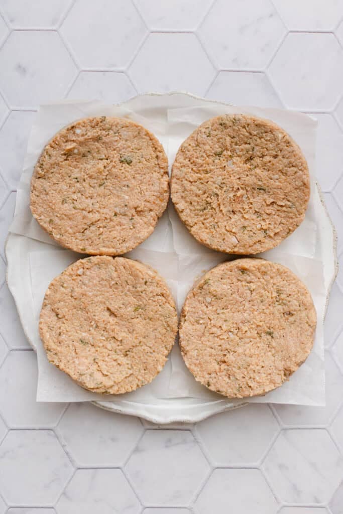 Uncooked, formed turkey burgers on a parchment paper lined plate. 