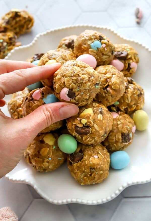 Hand grabbing a protein bites off of a plate full of more protein bites with Easter candy on it with them.