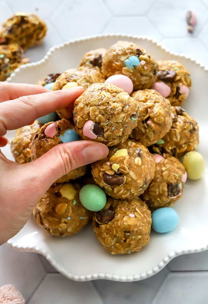 Hand grabbing a protein bites off of a plate full of more protein bites with Easter candy on it with them.