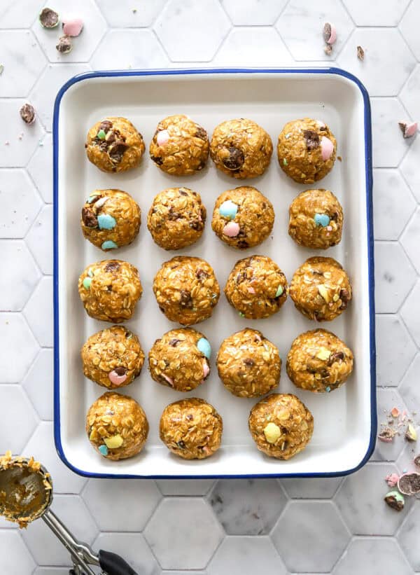 Tray of energy balls with a ice cream scoop with some of the mixture on it in front of it.