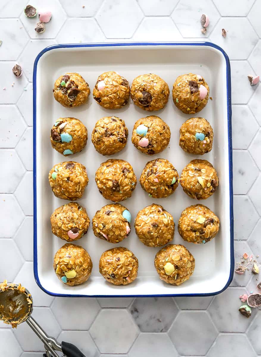 Tray of energy balls with a ice cream scoop with some of the mixture on it in front of it.