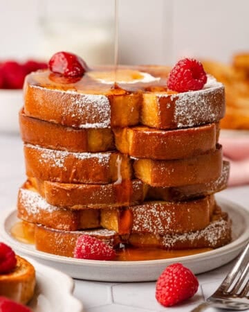 Stack of protein French toast with syrup being poured over it with berries on it.