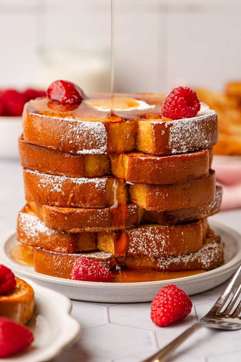 Stacked healthy french toast with syrup being poured over it with fresh raspberries on top. 