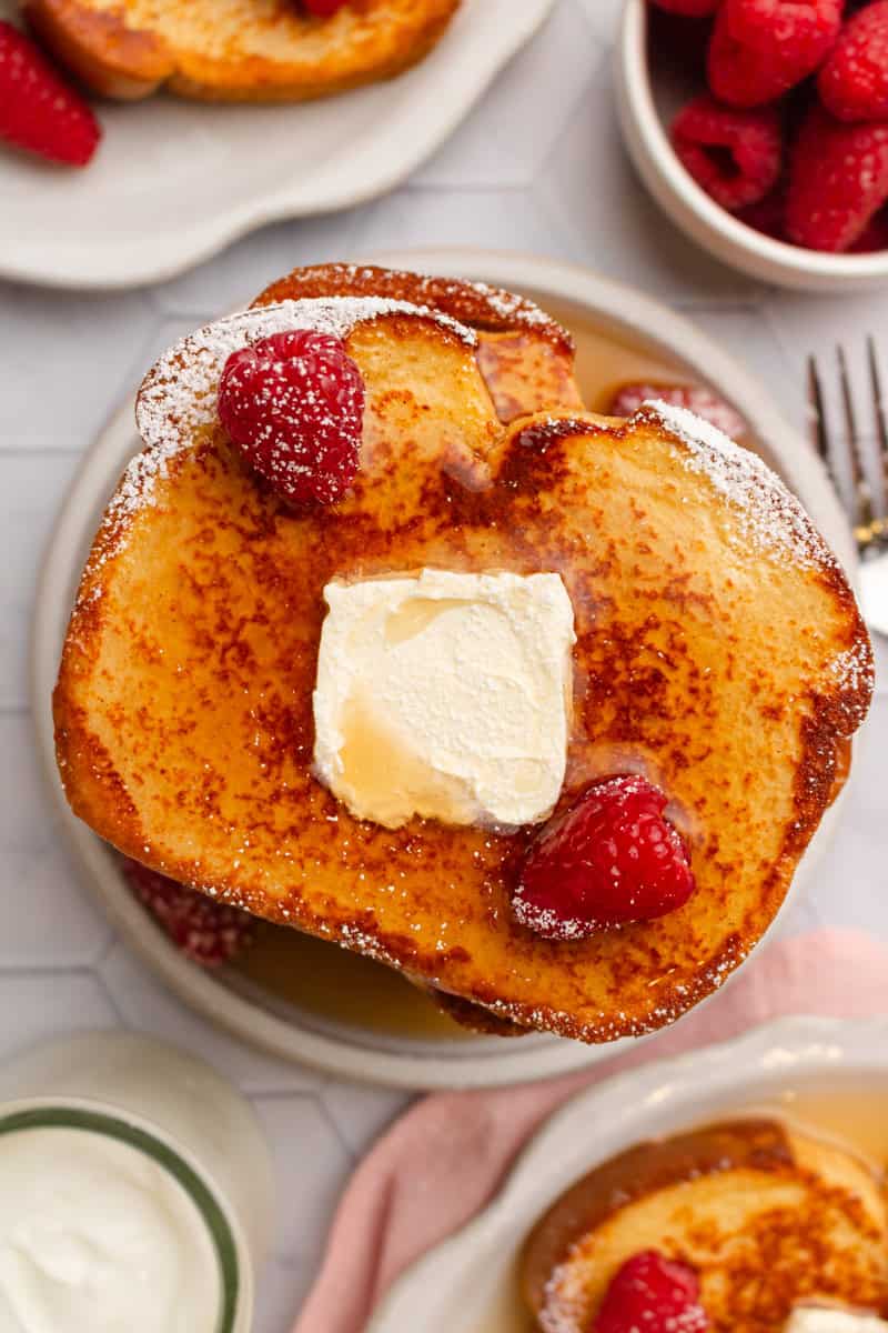 Healthy French toast with protein on a plate topped with maple syrup, butter, powdered sugar and berries. 