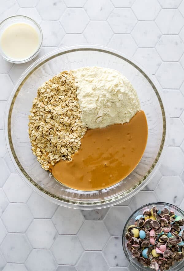 Protein ball ingredients in bowl before being mixed up with a bowl of chopped Cadbury eggs in front of it.