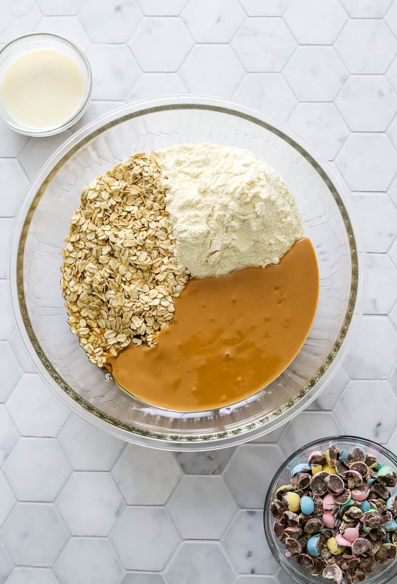 Protein ball ingredients in bowl before being mixed up with a bowl of chopped Cadbury eggs in front of it.