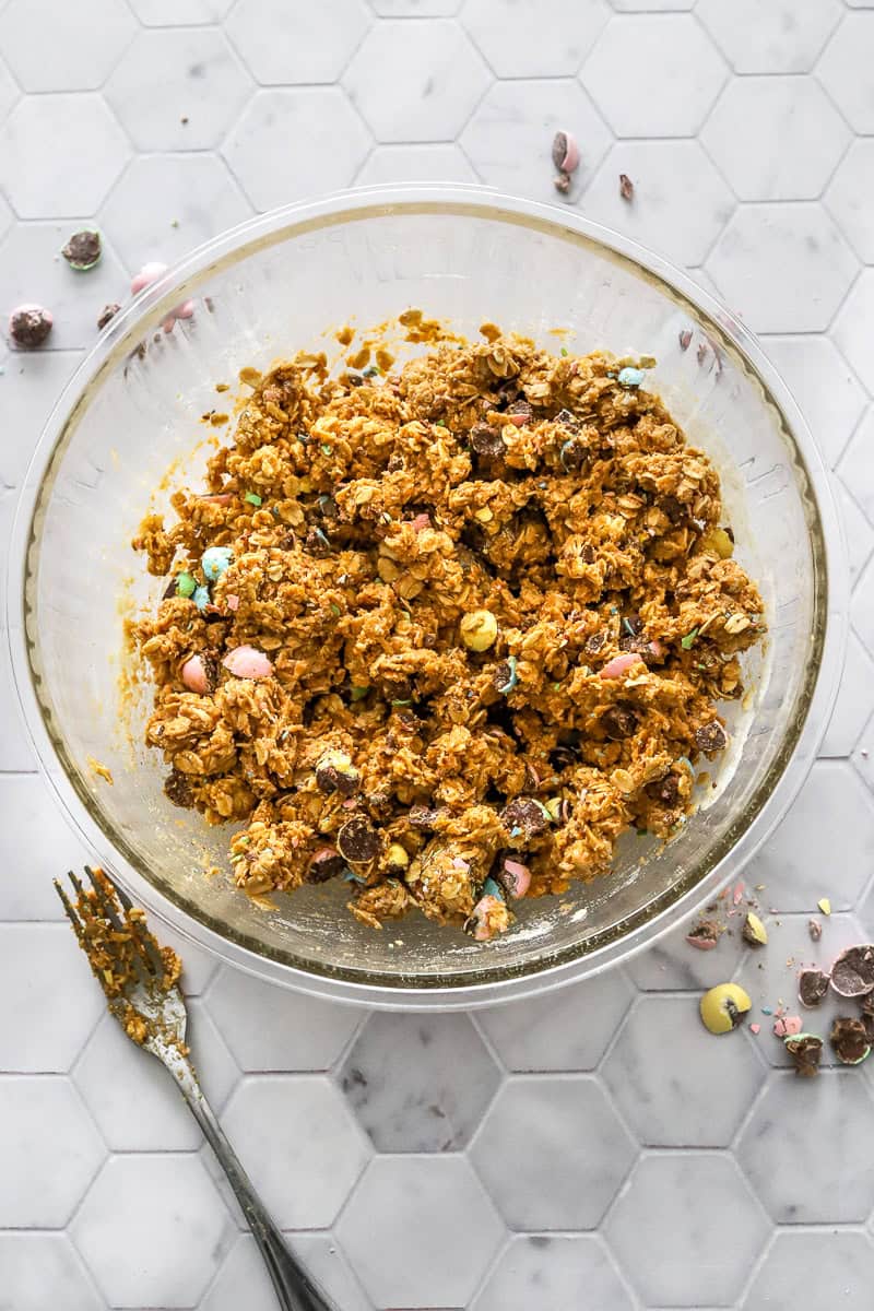 Mixture for Easter energy bites in a glass bowl with chopped Cadbury eggs around it.