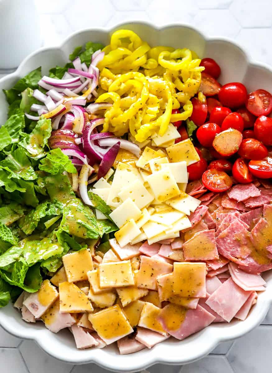 Chopped deli meats and cheese, lettuce, tomatoes, peppers and onion in a large salad bowl topped with dressing. 