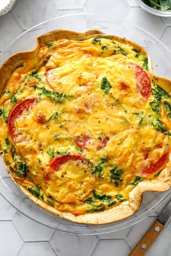 Baked cheesy tortilla quiche in glass pie dish with a knife in front of it.