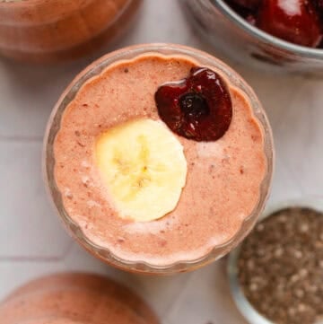 Cherry banana smoothie blended in a glass with another one in front of it and behind it.
