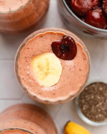 Cherry banana smoothie blended in a glass with another one in front of it and behind it.