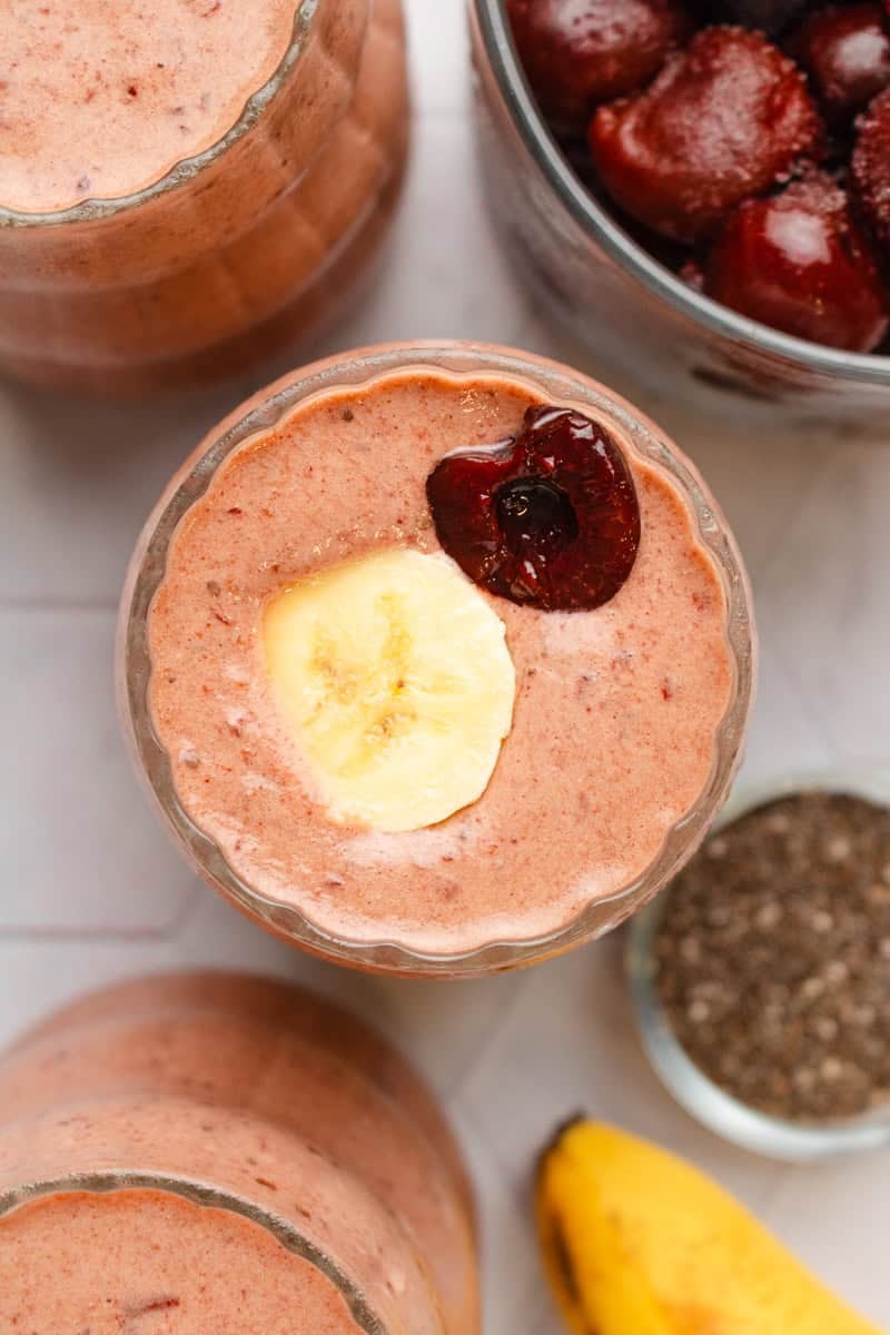 Cherry banana smoothie blended in a glass with another one in front of it and behind it.