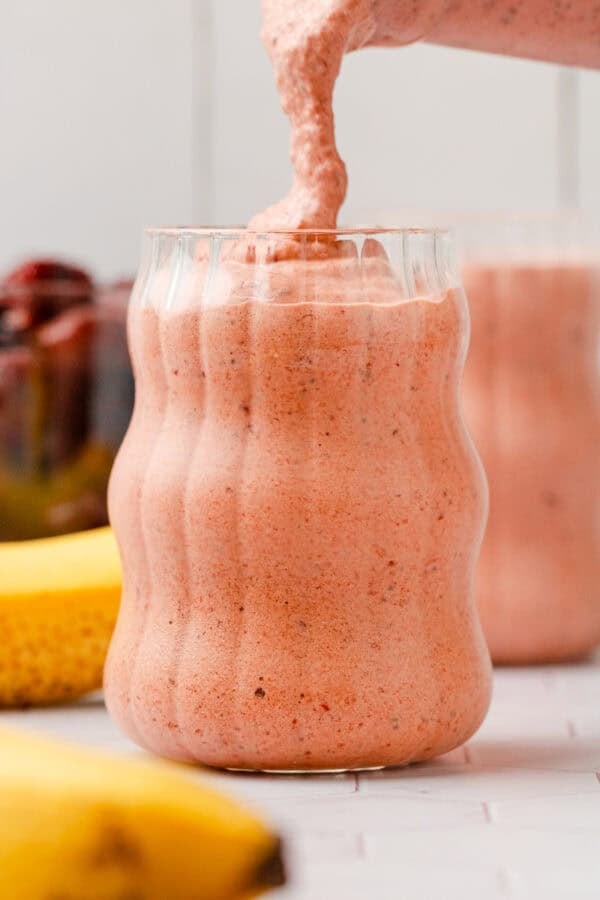 Pouring smoothie into glass with another one behind it.