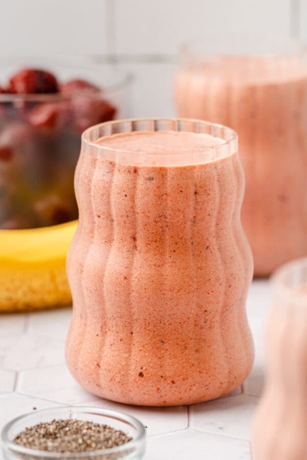 Banana smoothie with cherries in a glass with more smoothies in glasses around it.