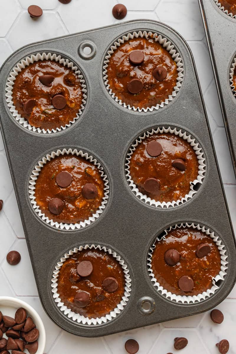 Chocolate muffin batter divided between lined muffin cups in a muffin pan. 