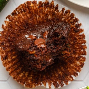 Zucchini chocolate muffin on paper with more zucchini around it.