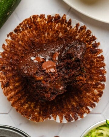 Zucchini chocolate muffin on paper with more zucchini around it.