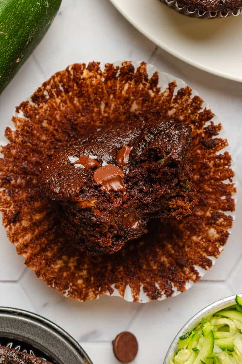 Zucchini chocolate muffin on paper with more zucchini around it.