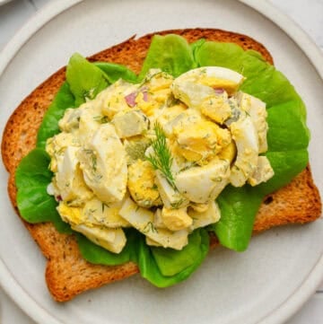 Healthy egg salad on whole grain toast on a plate.