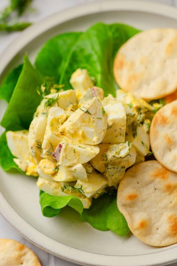 Creamy avocado mayo egg salad on a lettuce leave with crackers in front of it.