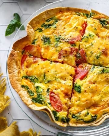 Tomato spinach tortilla quiche baked in a glass pie dish cut into portions.