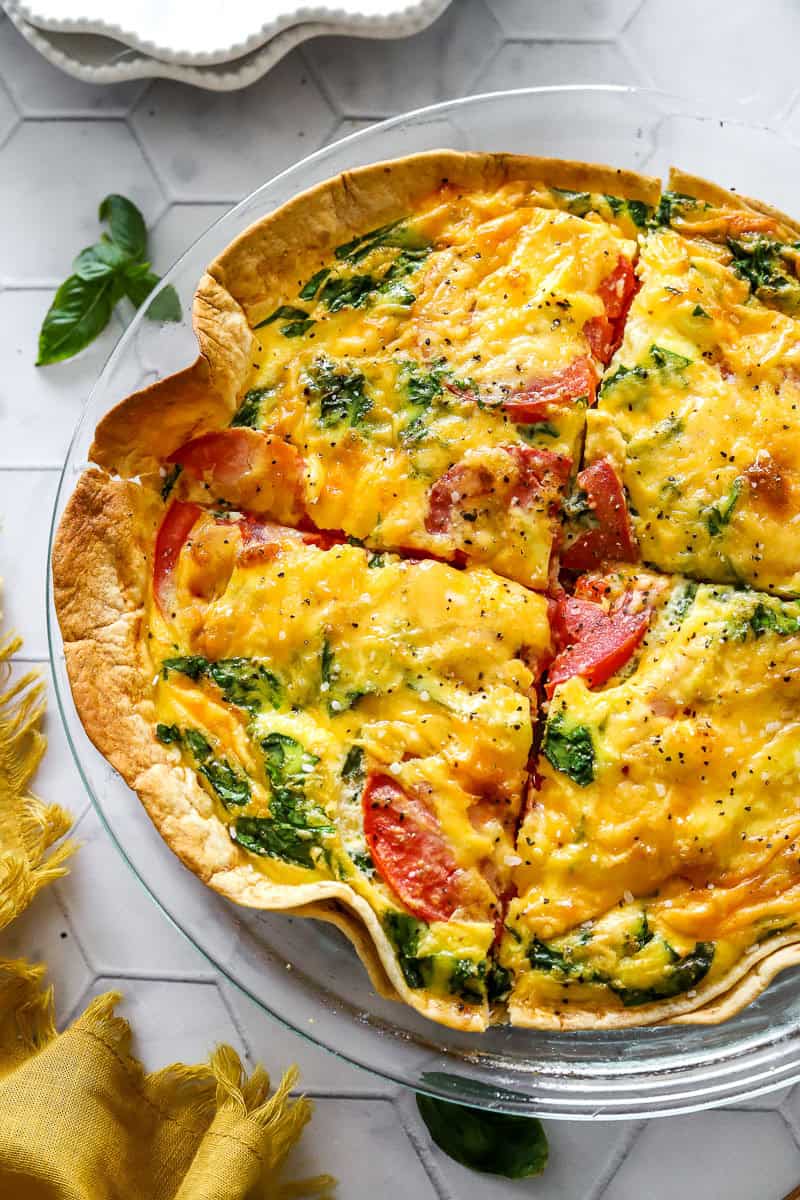 Tomato spinach tortilla quiche baked in a glass pie dish cut into portions.