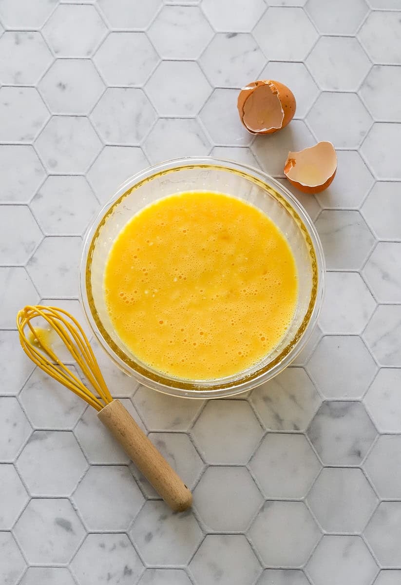 Whisked eggs and cottage cheese in a glass bowl with a yellow whisk in front of it.
