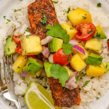 Salmon over rice with mango salad on top on a plate.