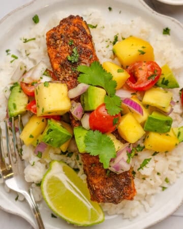 Salmon over rice with mango salad on top on a plate.