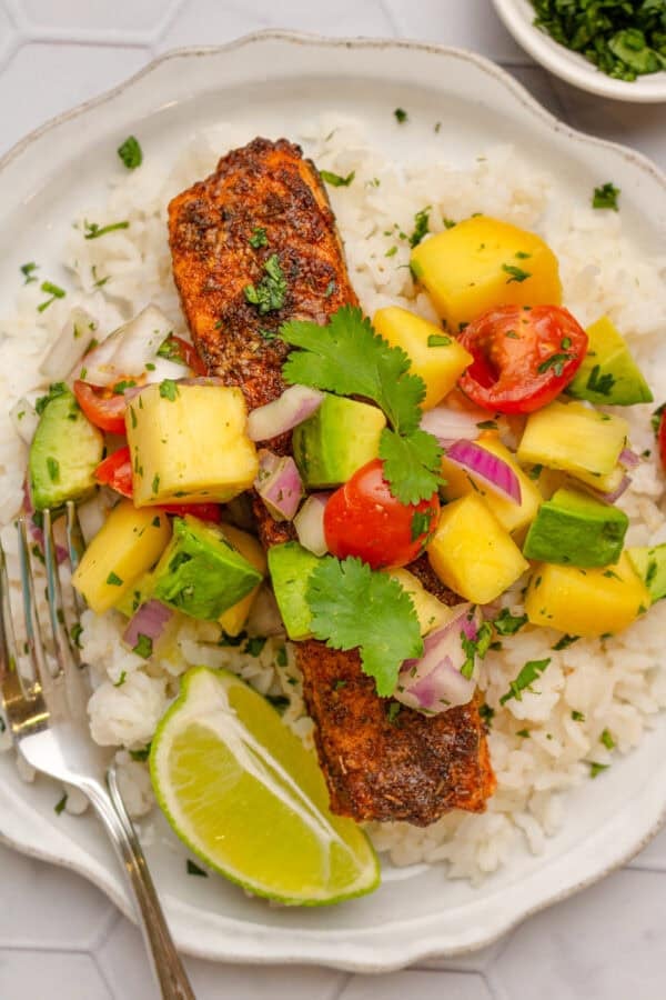 Salmon over rice with mango salad on top on a plate.