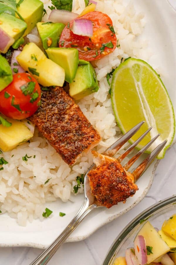 Cajun salmon over rice on a plate with a fork with some on it.