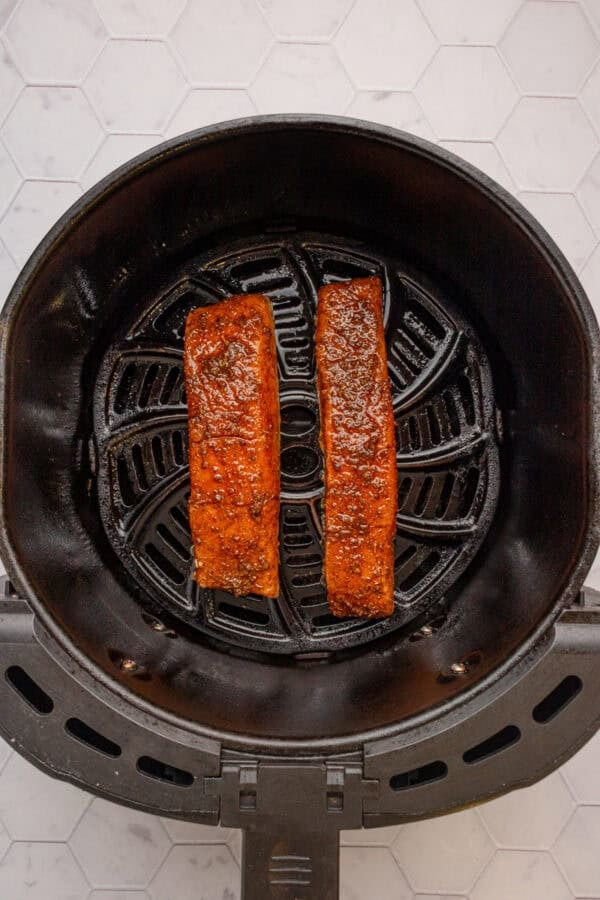 Raw cajun seasoned salmon in an air fryer basket.
