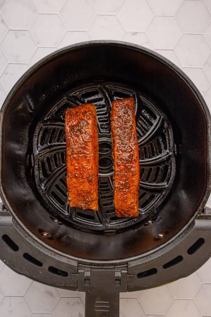 Raw cajun seasoned salmon in an air fryer basket. 