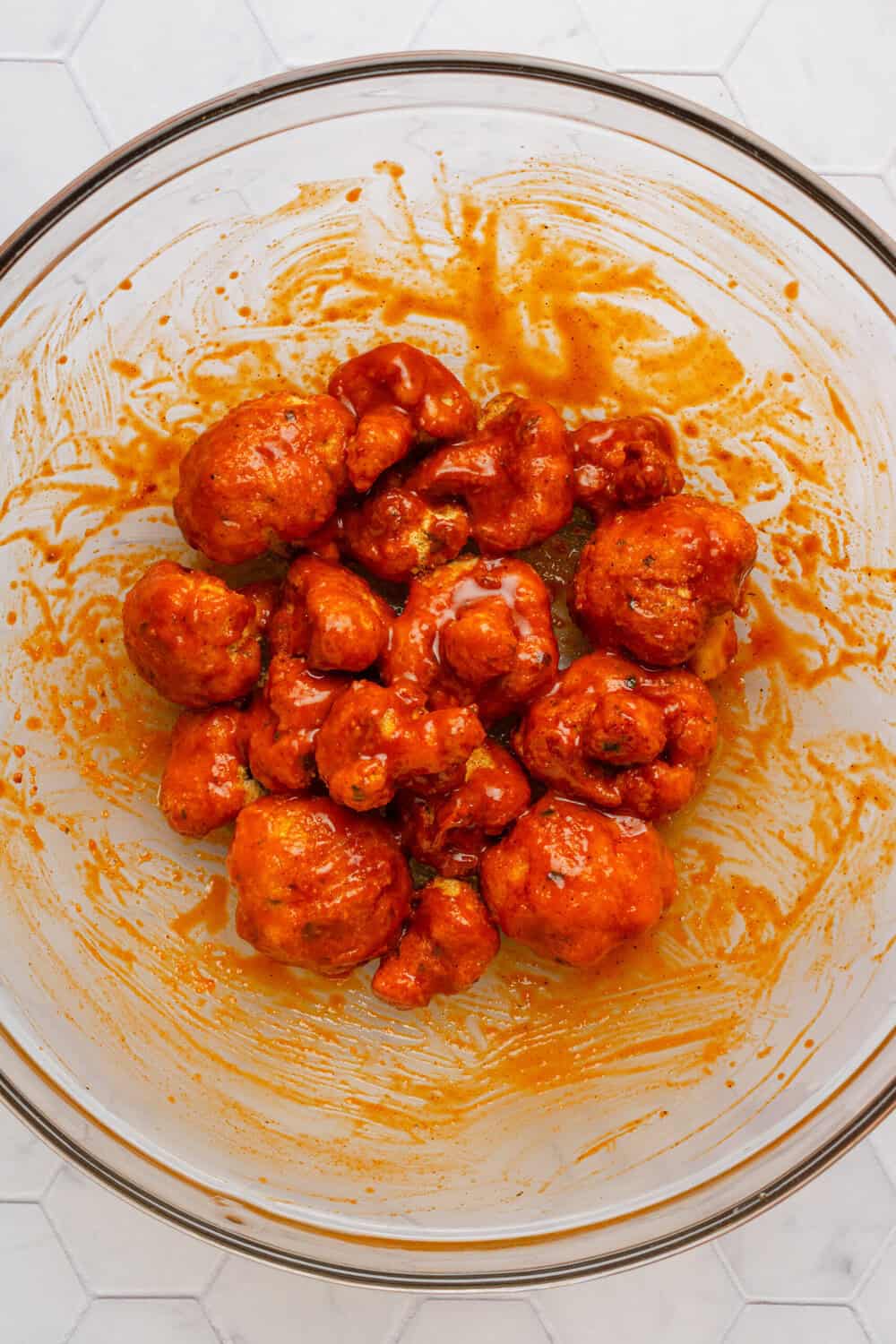 Air fried crispy cauliflower bites in a glass bowl tossed in buffalo sauce.