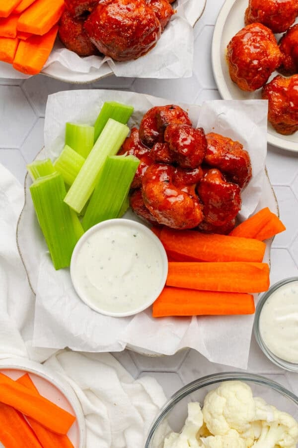 Plate of air fryer buffalo cauliflower with a cup of creamy dip and cut carrots and celery next to it with my plates of it around it.