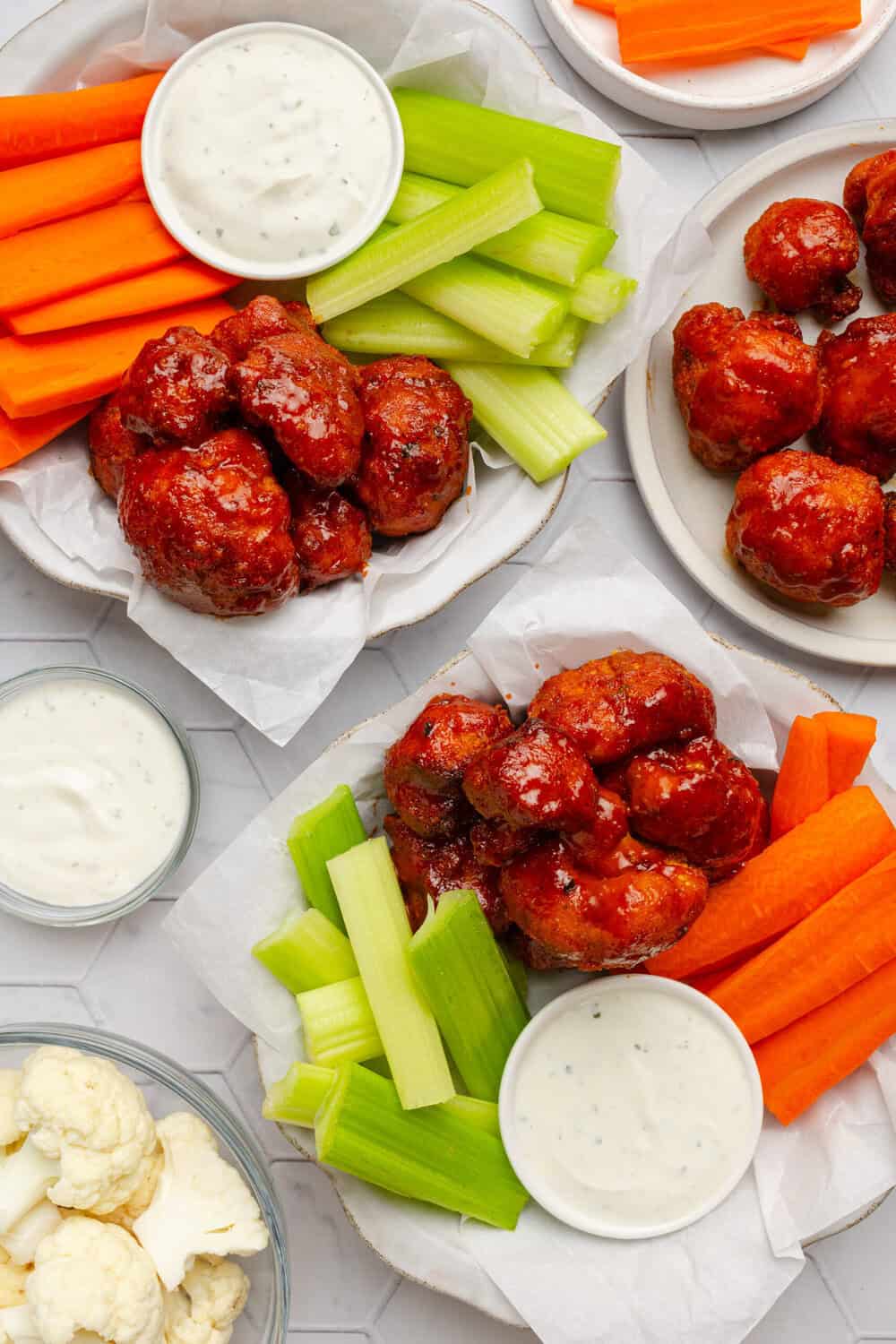 Plates filled with buffalo cauliflower wings with cut veggies and a small bowl of creamy dip on each plate with it.
