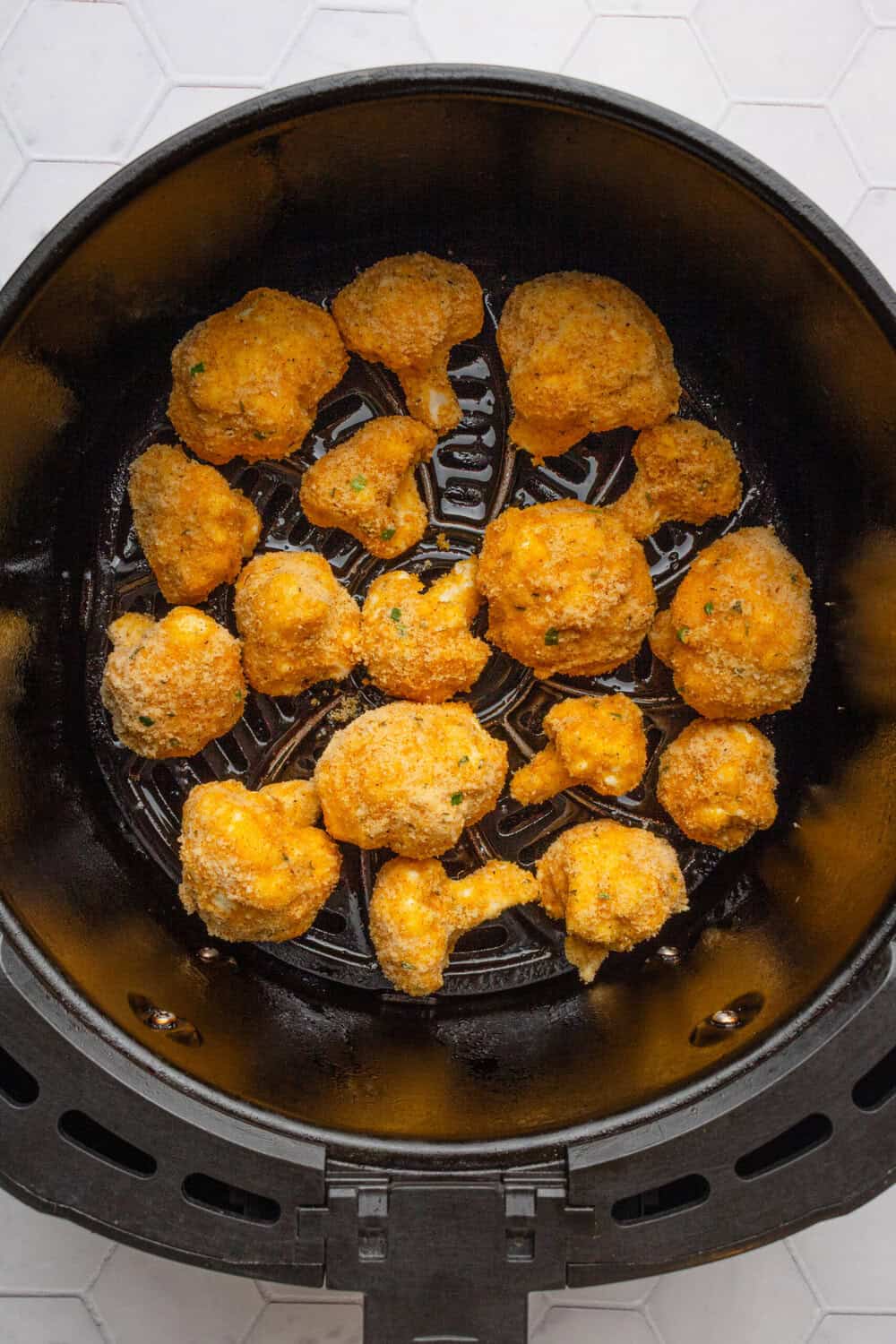 Breaded uncooked cauliflower in an air fryer basket.