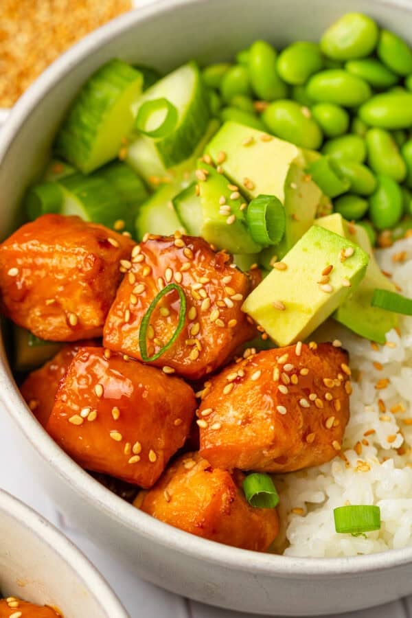 Cubed air frye salmon seasoned with teriyaki sauce in a bowl over rice and edamame and avocado.