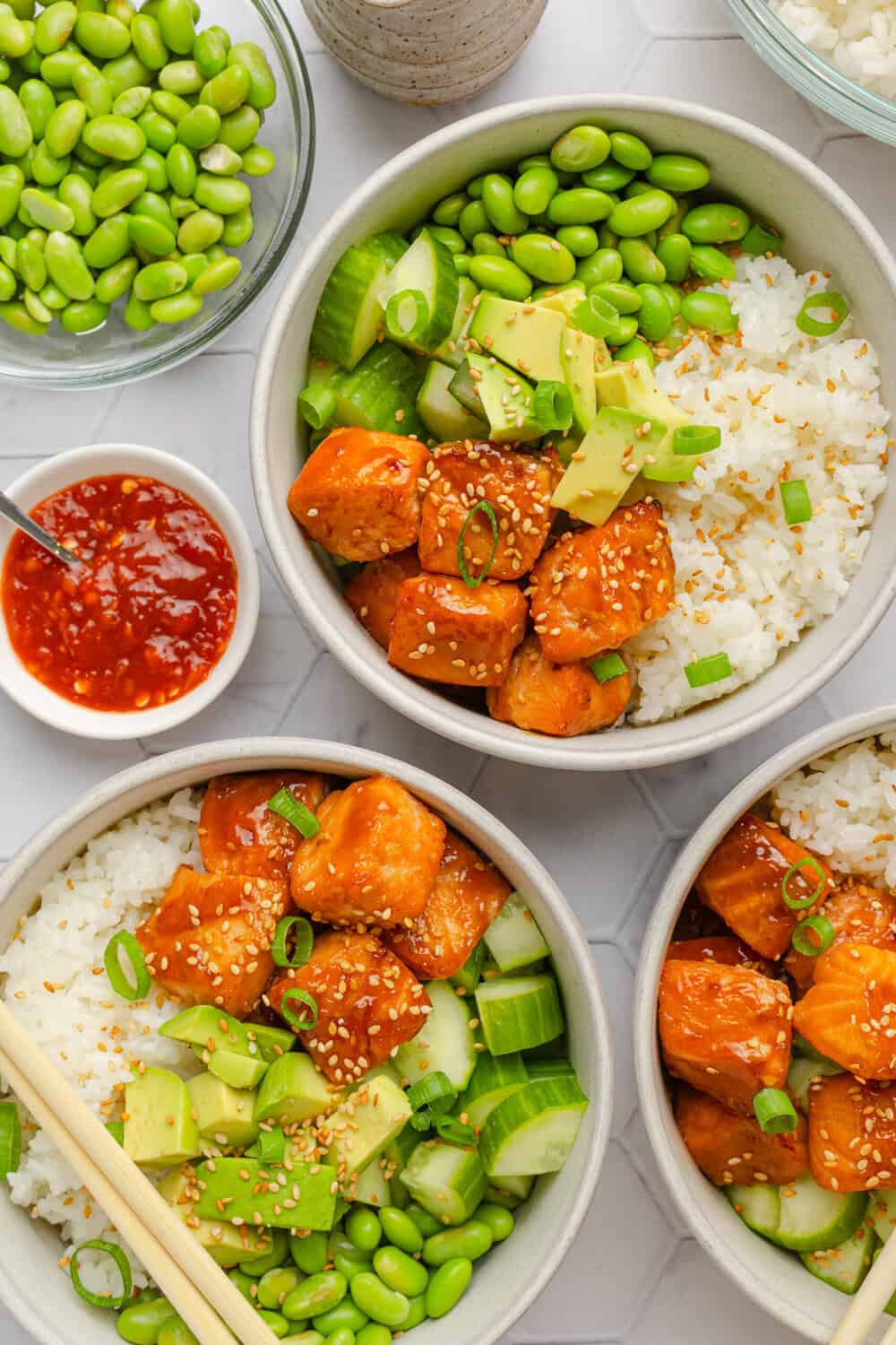 Three teriyaki salmon bowls with rice and veggies in each bowl with the salmon. 