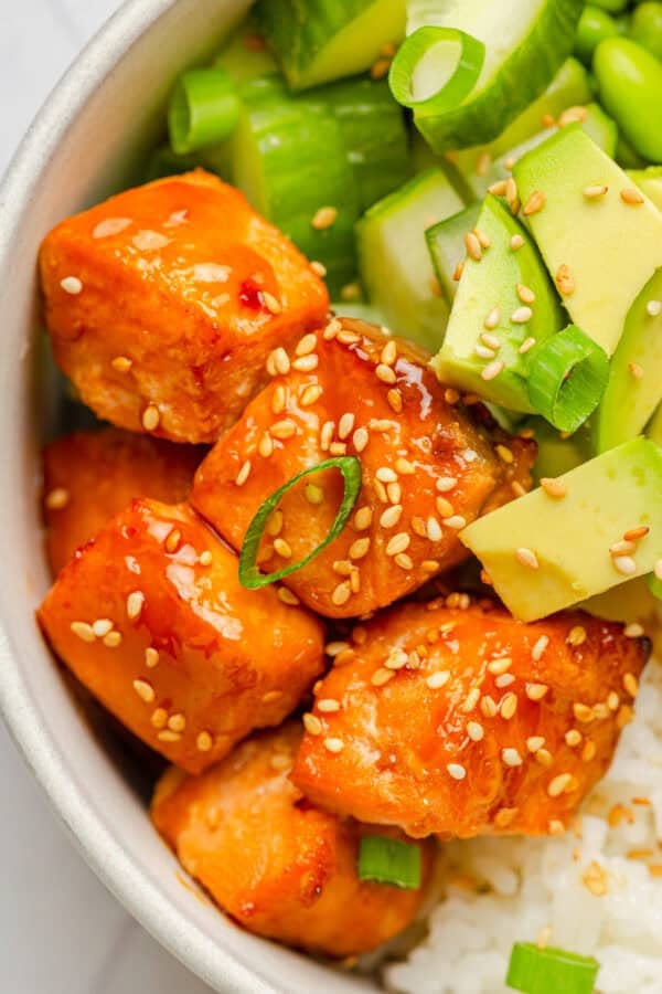 Cubed cooked seasoned teriyaki salmon over rice in a bowl topped with sesame seeds.
