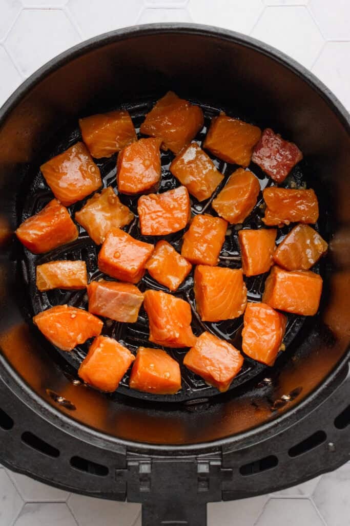 Raw teriyaki marinated salmon cubes in an air fryer basket.