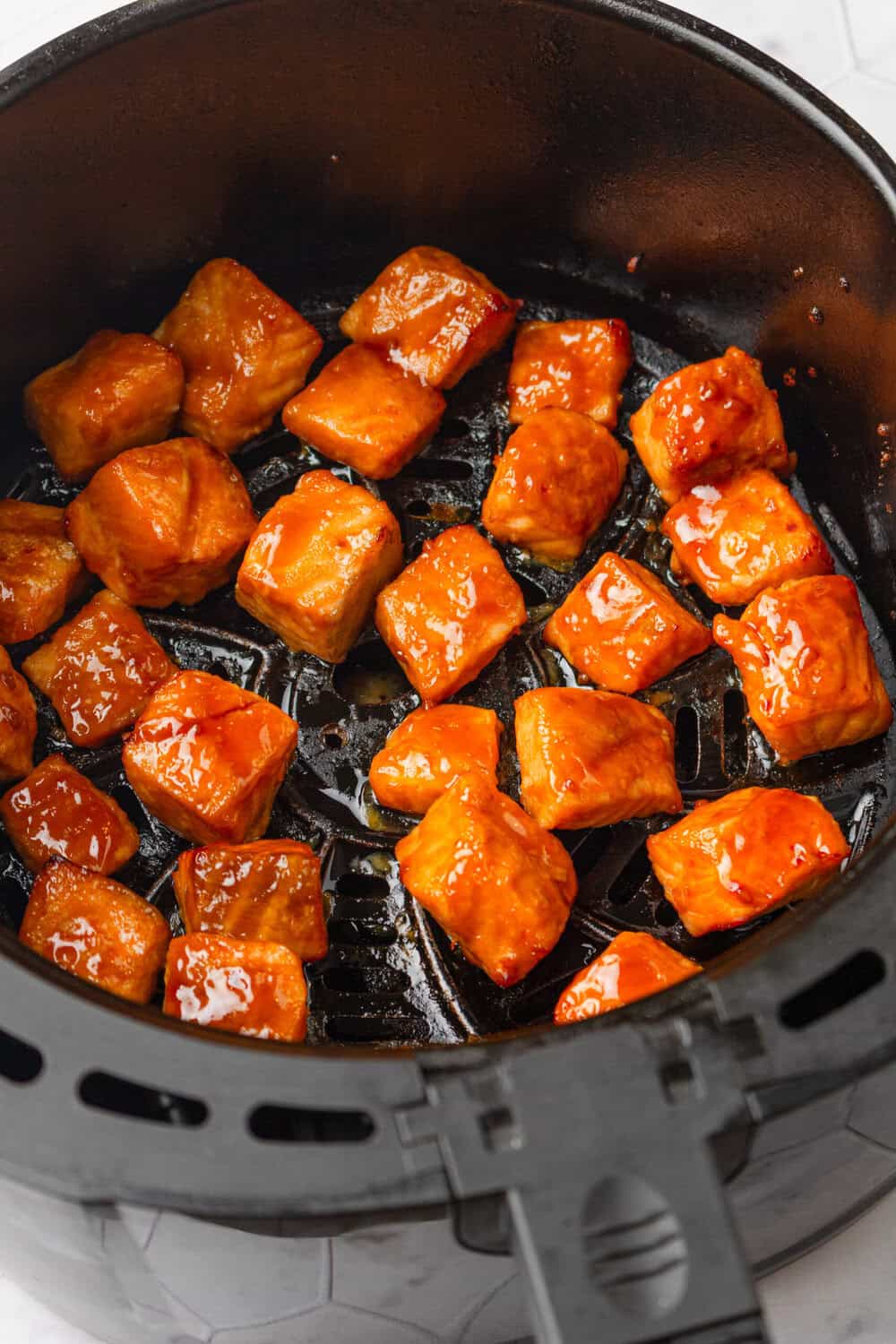 Cubed salmon bites covered in teriyaki sauce in an air fryer. 