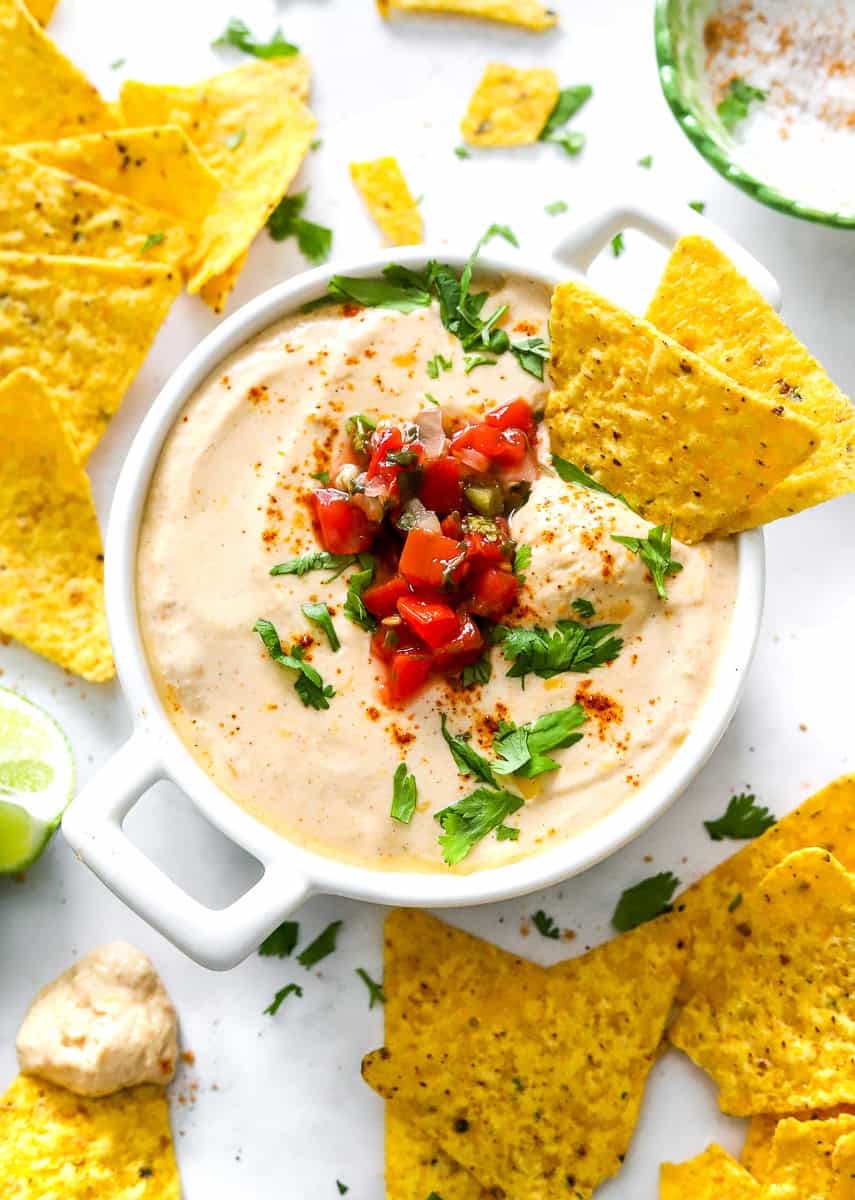Bowl of high protein queso dip with tortilla chips in it and around it.